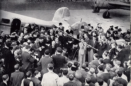 Extracted from the Woolworth's House Journal 'The New Bond' a picture of Prime Minister Neville Chamberlain amidst a throng on the tarmac at Heston Aerodrome in Croydon with his piece of paper. The picture carries the single word caption 'Peace!'