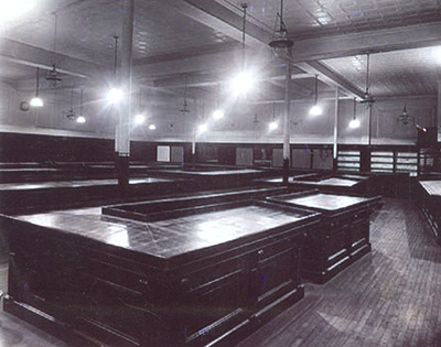 An unusual view showing the salesfloor about a week before the store opened. Lighting (both 150W incandescent and gas for emergencies has been installed, along with the cornices and elegant gold and red diamond W chains above them (an early corporate ID), with the mahogany counters and wall treatment in place, ready for the glass dividers to be added to the counter-tops and the merchandise to be laid out and ticketed